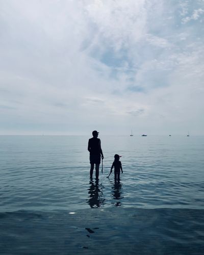 A person and a child are standing in the sea.